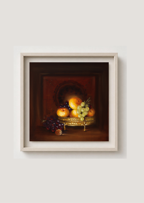 A framed still life painting of fruit, featuring oranges, grapes, and a pear on a gold tray, set against a dark brown background. The artwork is housed in a light beige frame and is mounted on a neutral light gray wall. Abundance - original chiaroscuro oil painting of a gilded fruit bowl with oranges and grapes by Marta Stolarska