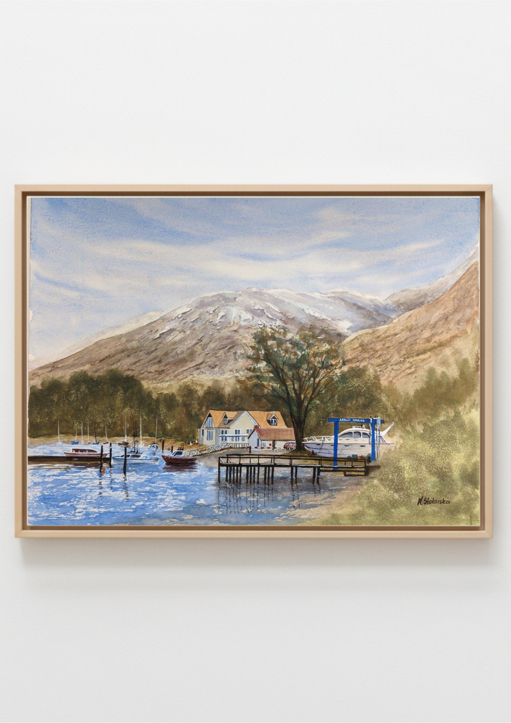 A framed landscape painting depicting a scenic lake with boats, a pier, small houses, trees, and a large snow-dusted mountain under a cloudy sky, shown against a plain light background. Painting of a lakeside scene with a house, dock, and mountains. Original watercolour painting of Ardlui Marina Loch Lomond Scottish Highlands, inspired by first trip to Scotland