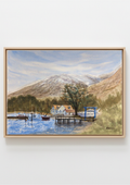 A framed landscape painting depicting a scenic lake with boats, a pier, small houses, trees, and a large snow-dusted mountain under a cloudy sky, shown against a plain light background. Painting of a lakeside scene with a house, dock, and mountains. Original watercolour painting of Ardlui Marina Loch Lomond Scottish Highlands, inspired by first trip to Scotland