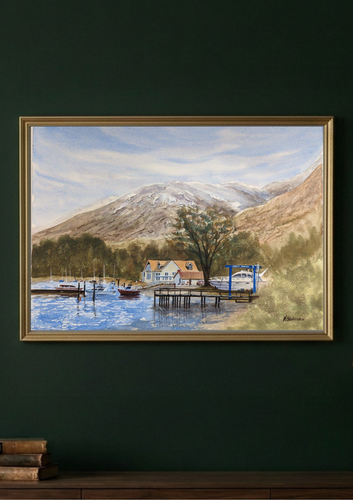 A framed landscape painting of a mountain lake scene with boats, docks, and small buildings, displayed on a dark green wall above a wooden surface.