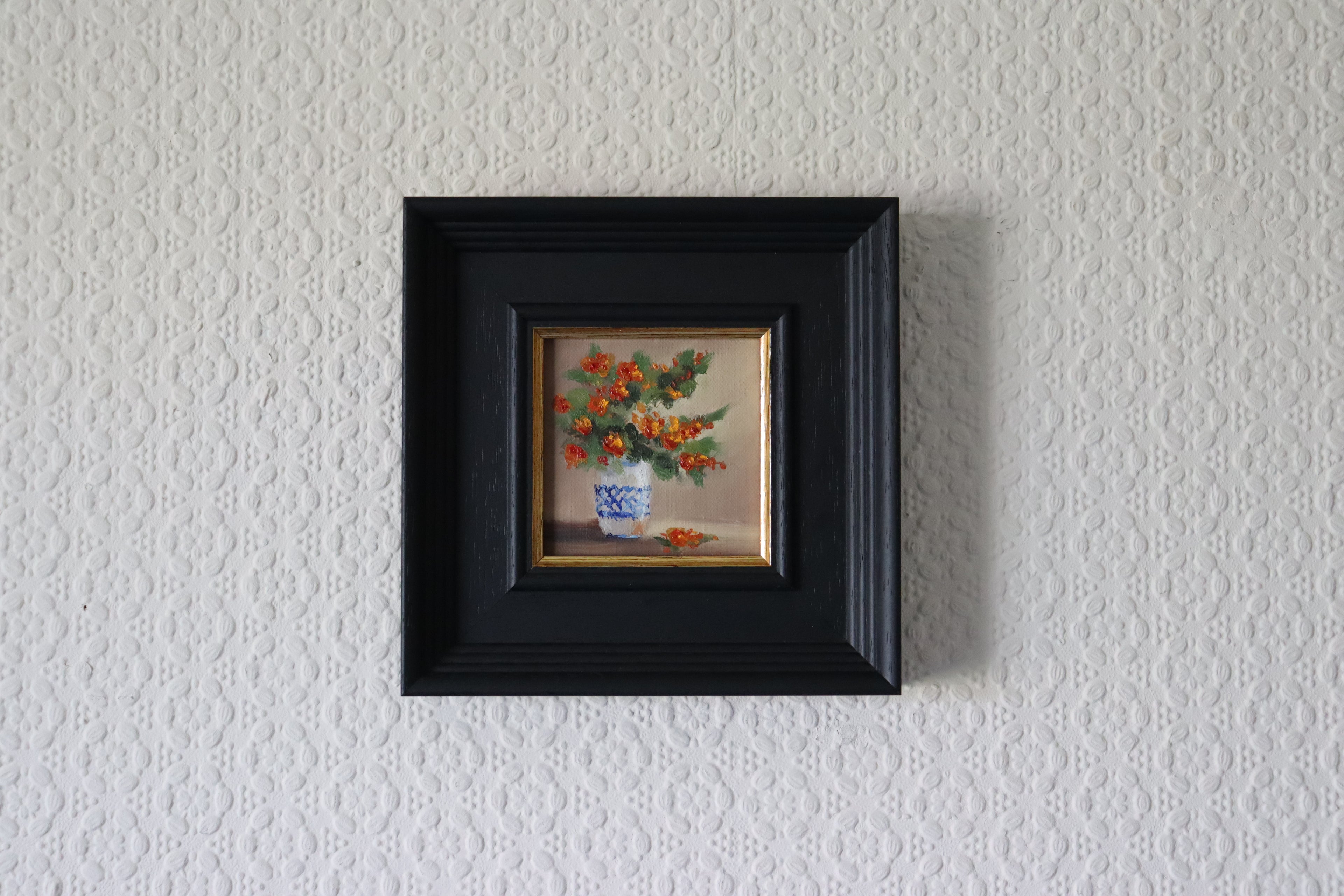 Small framed painting of a floral arrangement on a textured white wall. Original oil painting of an autumnal trio of flowers or fruits, warm amber and rust tones still life