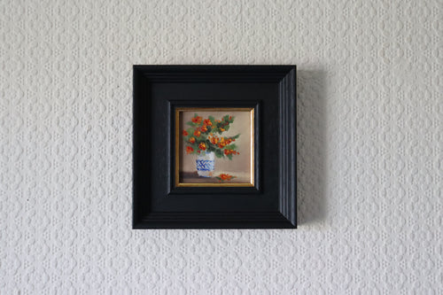 Small framed painting of a floral arrangement on a textured white wall. Original oil painting of an autumnal trio of flowers or fruits, warm amber and rust tones still life