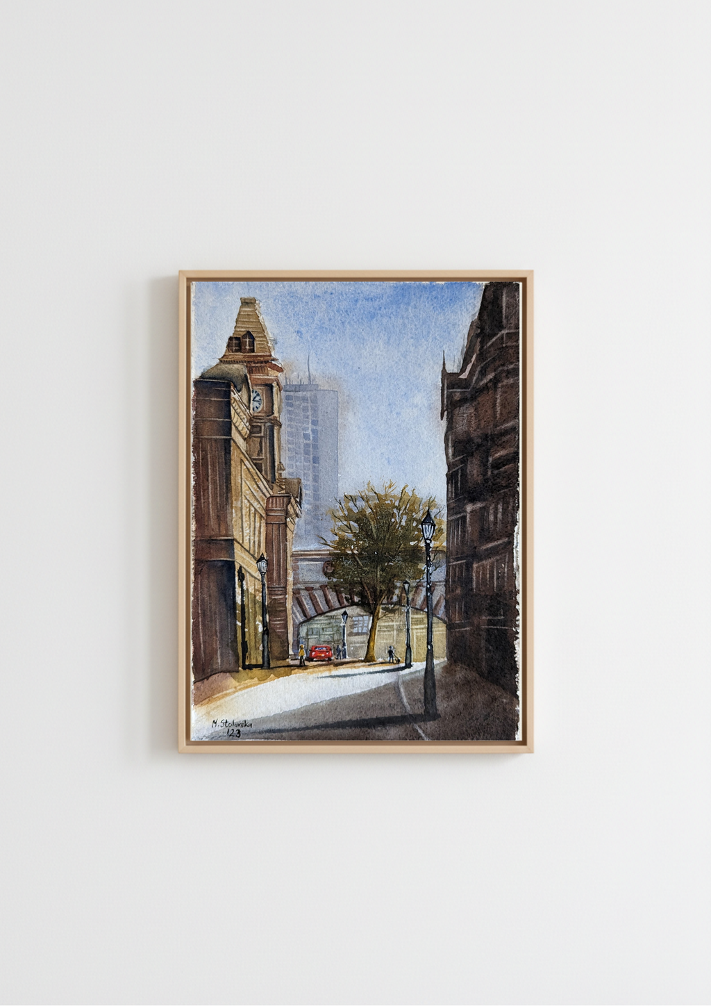 A framed watercolor painting of a city street scene with buildings, a tree, and a red car, displayed on a clean white wall. Birmingham Museum and Art Gallery from Edmund Street - limited edition fine art print by Marta Stolarska, based on original watercolour, A4 archival matt paper, edition of 50, hand signed and numbered