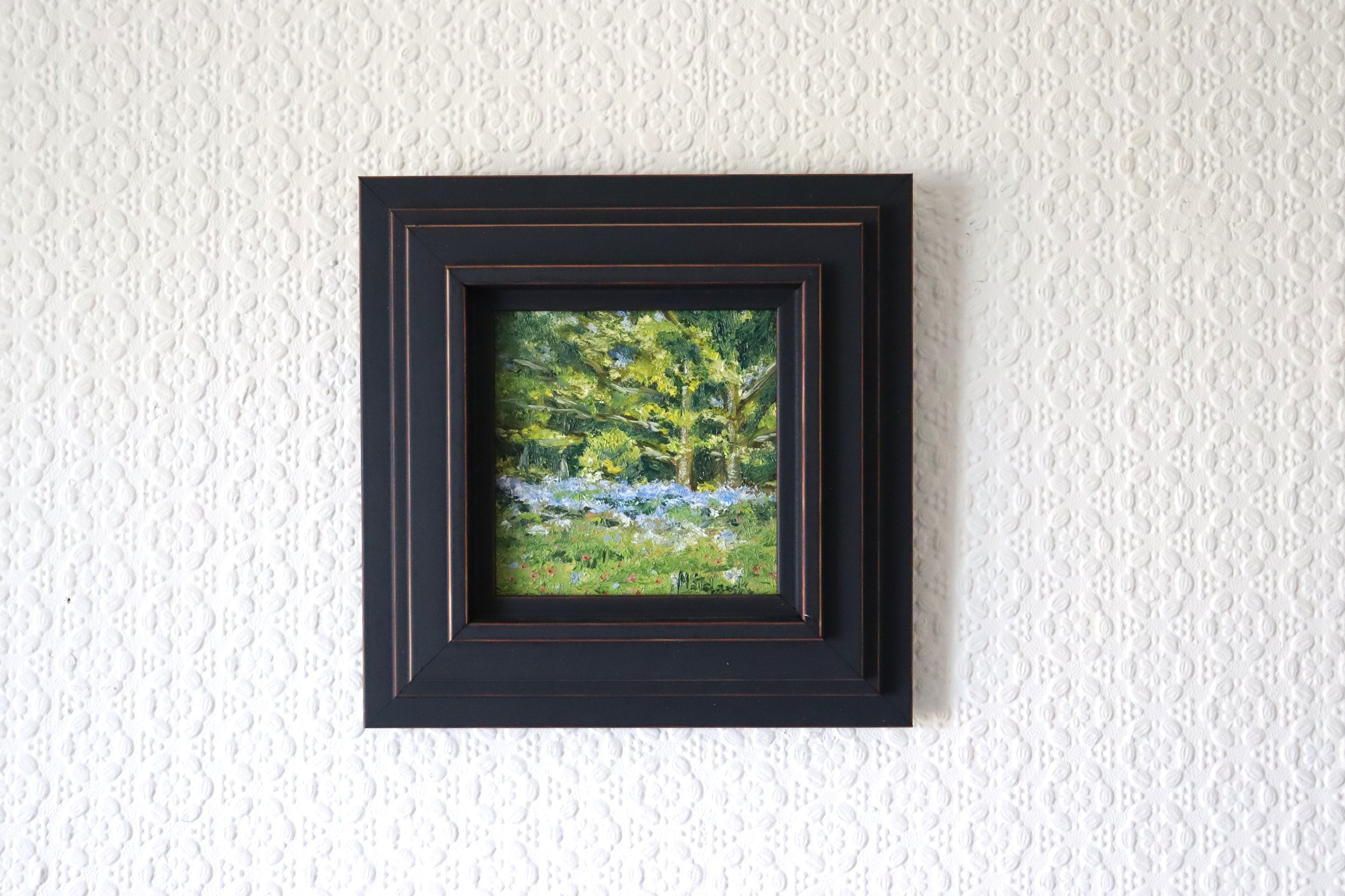 Framed, lifestyle setting of an Original plein air oil painting of bluebells on Beacon Hill Lickey Hills Birmingham, painted from life in spring. artwork of a forest scene on a textured white wall