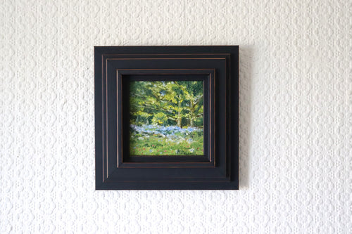 Framed, lifestyle setting of an Original plein air oil painting of bluebells on Beacon Hill Lickey Hills Birmingham, painted from life in spring. artwork of a forest scene on a textured white wall