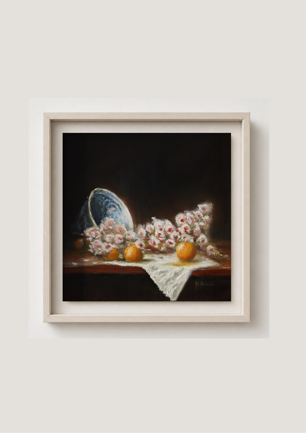 A framed still life painting featuring pink flowers, orange fruits, and a blue-and-white porcelain dish on a dark background, displayed against a light beige wall. Blossom and Oranges - original oil still life by Marta Stolarska, spring blossom in old white and blue porcelain bowl with glowing oranges on white linen cloth, oil on cradled wooden panel, 30x30cm