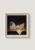 A framed still life painting featuring pink flowers, orange fruits, and a blue-and-white porcelain dish on a dark background, displayed against a light beige wall. Blossom and Oranges - original oil still life by Marta Stolarska, spring blossom in old white and blue porcelain bowl with glowing oranges on white linen cloth, oil on cradled wooden panel, 30x30cm