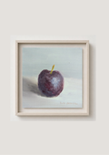 A framed still life painting of a dark purple plum with a small yellow stem, set against a pale blue-gray background. The artwork is housed in a light beige wooden frame and is mounted on a neutral light gray wall.