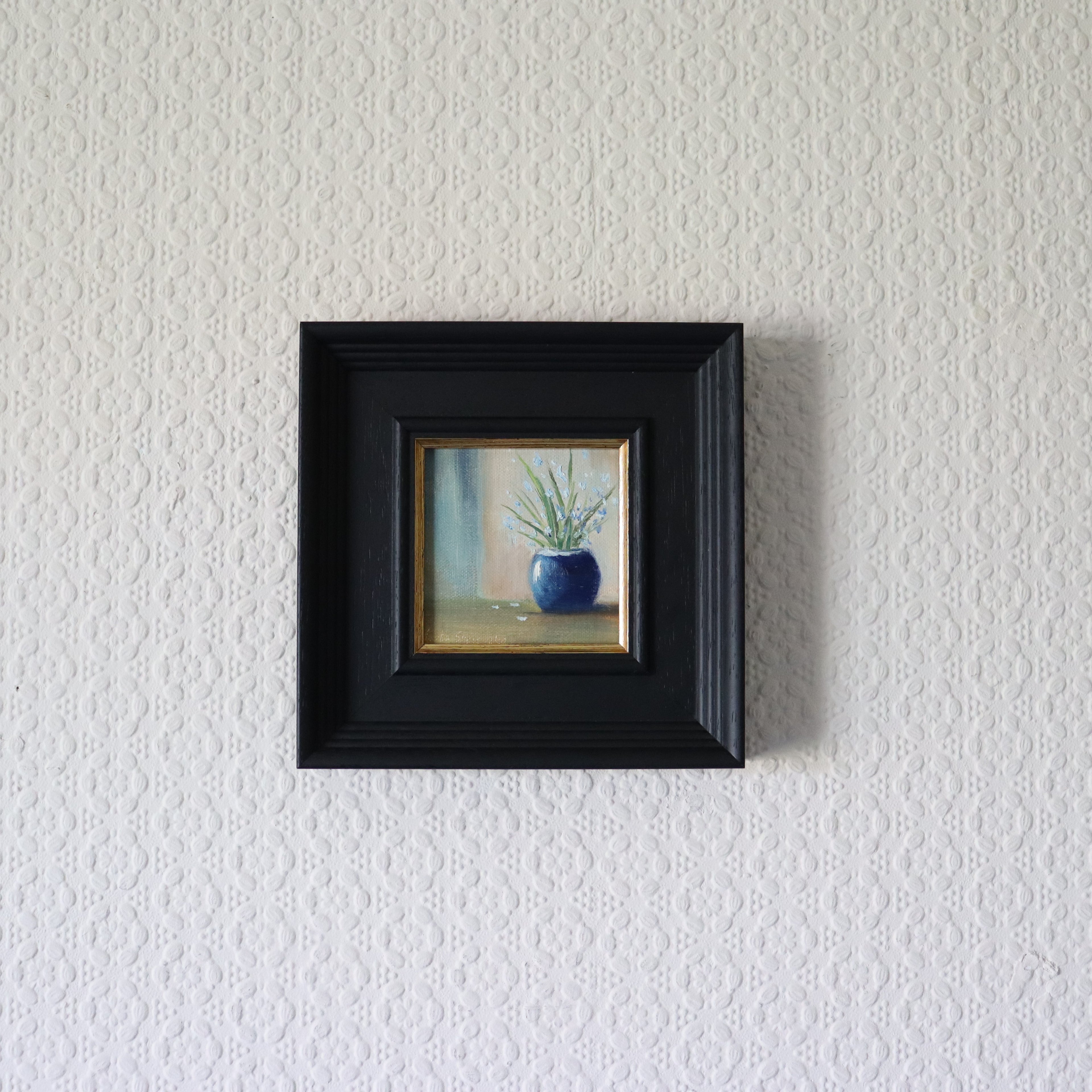 Small framed painting of a blue vase with plants on a textured white wall. Original oil painting of blue sparkles, shimmering blue vase with delicate flowers by Marta Stolarska