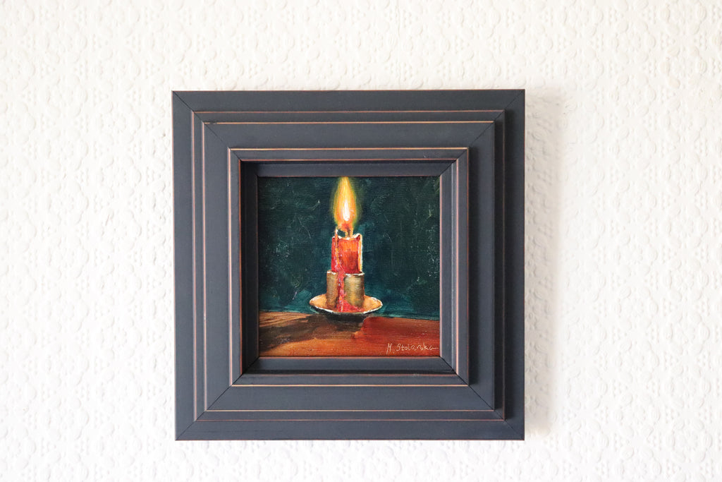 Framed painting of a candle on a textured wall. Original oil Painting of a lit red candle on a dark green background on a cradled panel. 