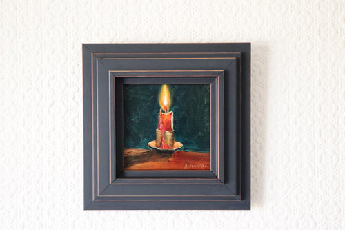 Framed painting of a candle on a textured wall. Original oil Painting of a lit red candle on a dark green background on a cradled panel. 