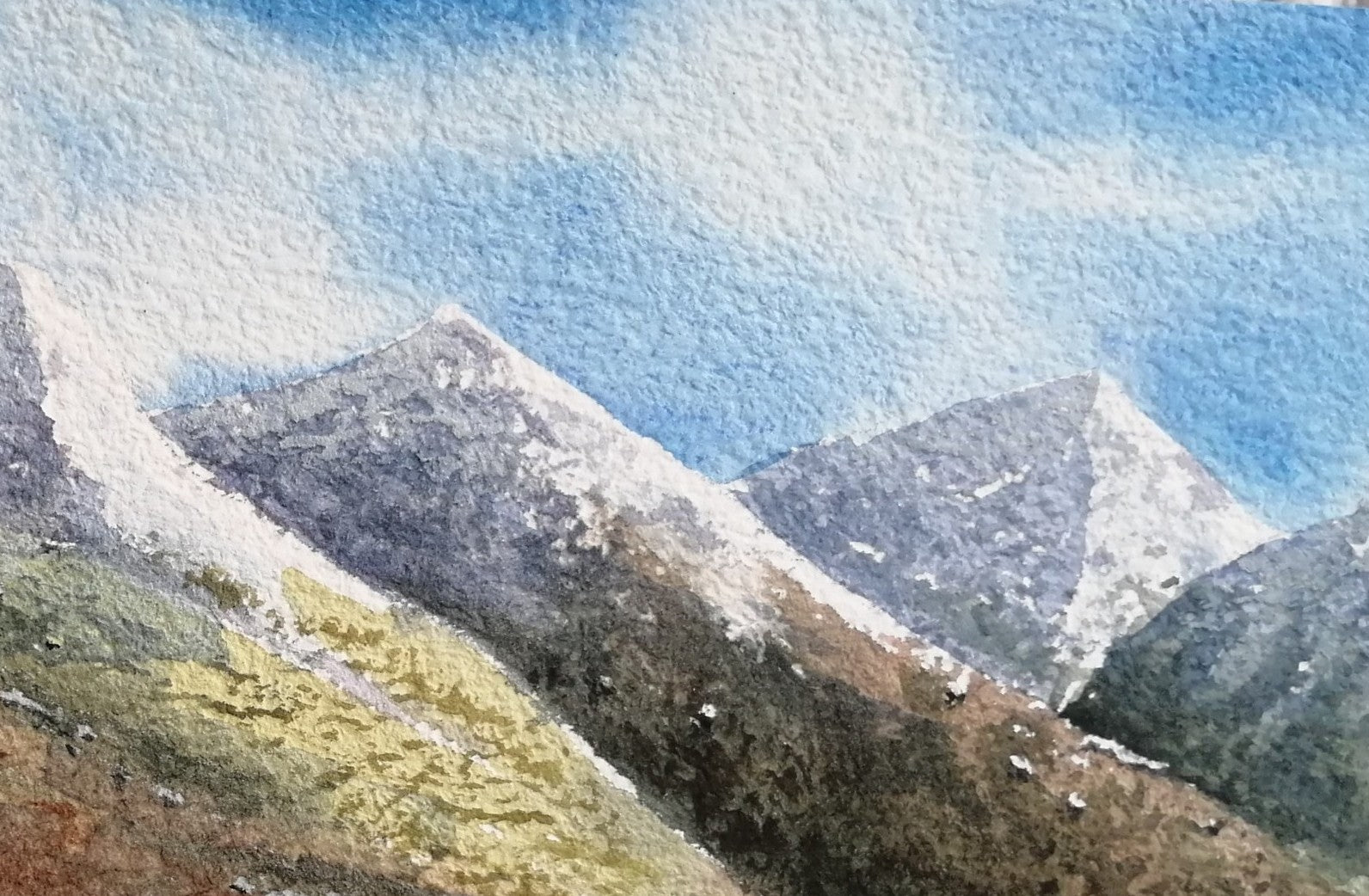 Mountain landscape with snow-capped peaks and a blue sky. Original watercolour painting of Castlerigg Stone Circle with snow-capped Lake District fells behind, light airy sky