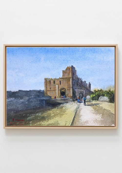A framed watercolor painting of a historic stone archway or gatehouse under a blue sky, with a path in the foreground and small figures near the entrance, shown against a light neutral wall. Painting of a castle with people walking towards it on a path. Original watercolour painting of Chepstow Castle great tower viewed from within the castle grounds, Wales