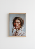 A framed portrait painting of a young woman with brown hair, blue eyes, and a white ruffled collar, hanging on a plain white wall. Composed - original oil portrait by Marta Stolarska, dark-haired woman with blue eyes and glowing skin in white high-collar shirt with gold dangling earring, oil on canvas board, Subtle Expressions collection