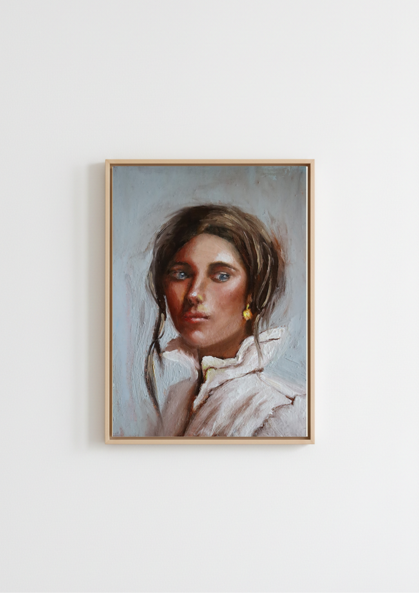 A framed portrait painting of a young woman with brown hair, blue eyes, and a white ruffled collar, hanging on a plain white wall. Composed - original oil portrait by Marta Stolarska, dark-haired woman with blue eyes and glowing skin in white high-collar shirt with gold dangling earring, oil on canvas board, Subtle Expressions collection
