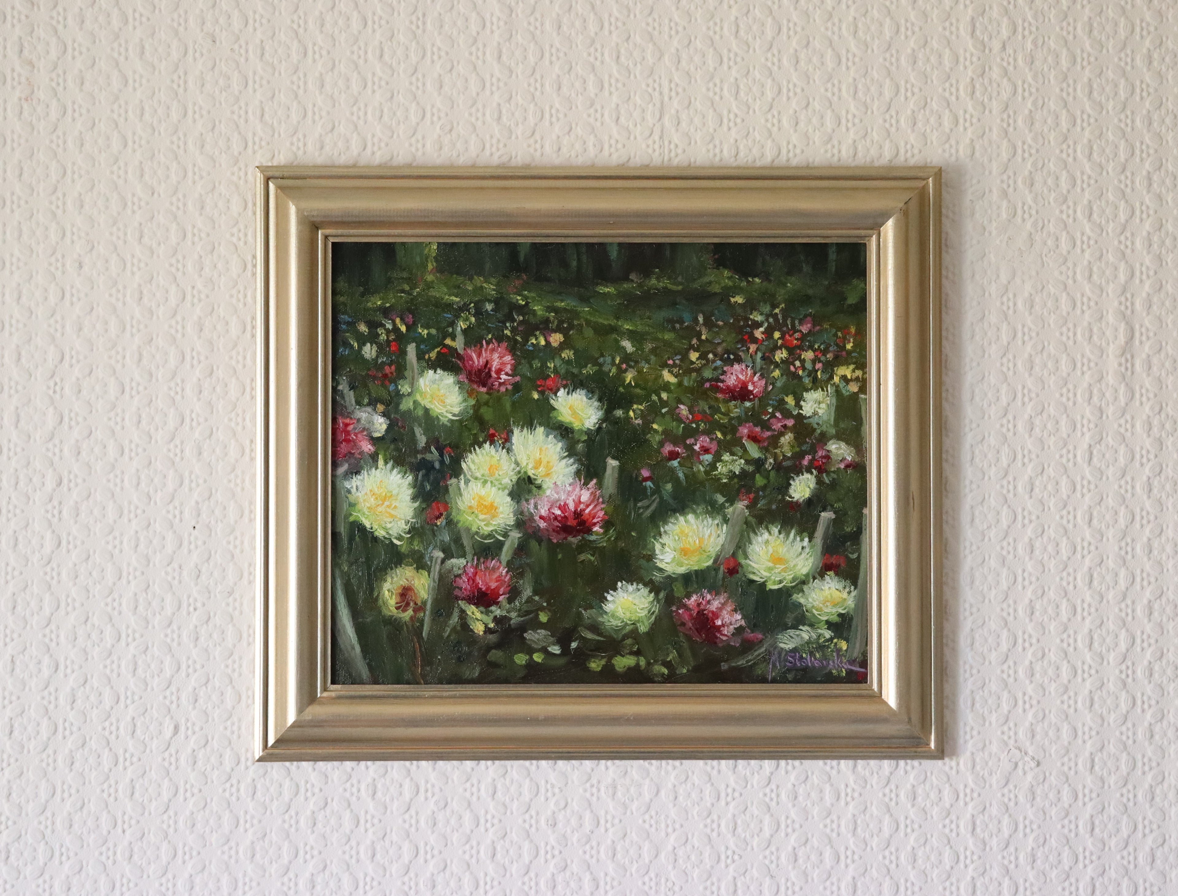 Framed in a gold wooden frame a painting of a floral garden on a textured wall. An original oil painting depicting a field of multicoloured dahlia flowers