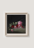 A framed still life painting featuring red roses, green leaves, and a pink glass cup on a dark background, presented in a light wood frame against a neutral wall. Darkness and Roses - original oil still life by Marta Stolarska, red roses and small pink jewellery pot emerging from darkness with strategic light, chiaroscuro painting on cradled wooden panel, 30x30cm