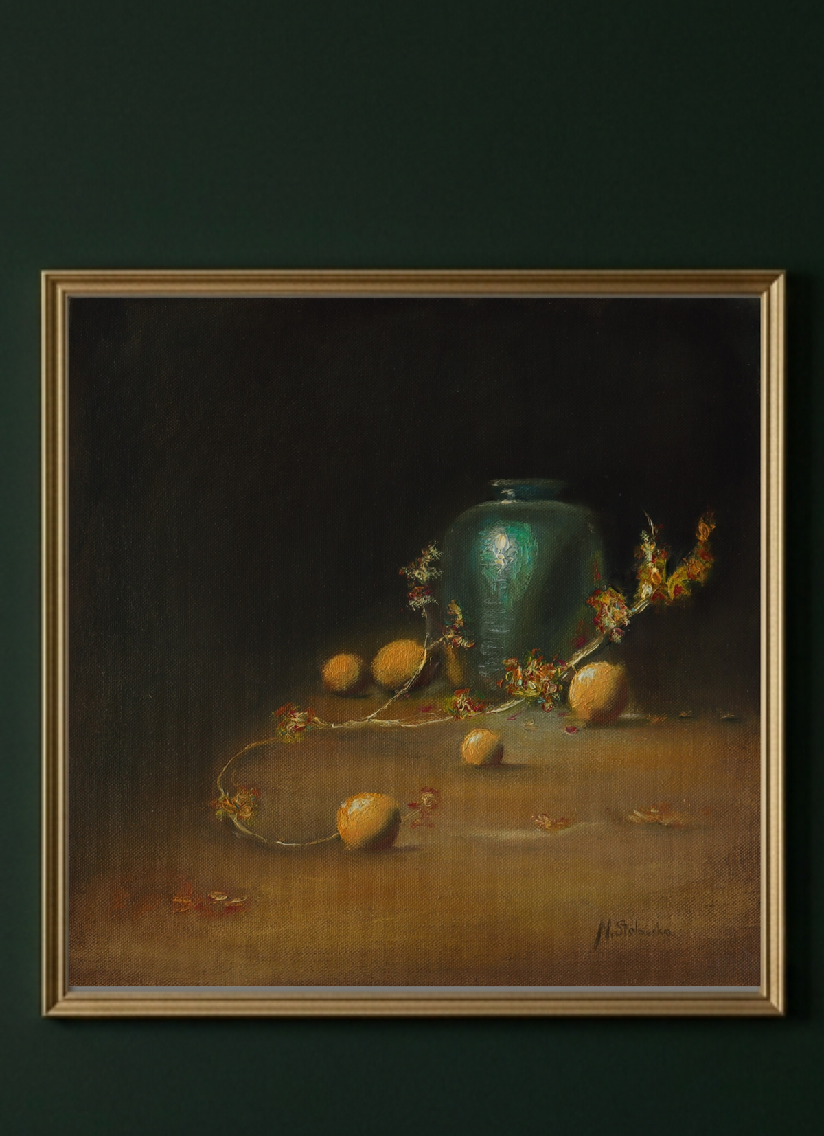 A framed still life painting featuring a dark green glass vase with yellow fruits and dried flowers on a dark brown and black background, set against a dark green wall.