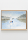 A framed watercolor painting of a sailboat on a calm lake with misty hills in the background, presented in a light wood frame against a white wall.