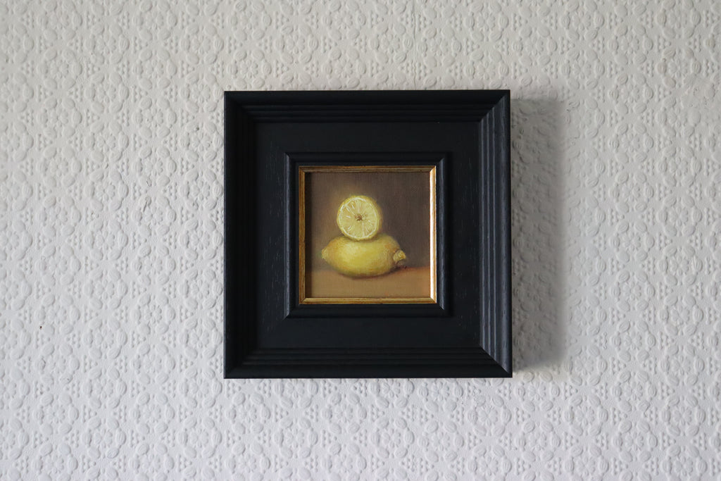 Framed artwork of a lemon on a textured wall. A painting of a very bright lemon with purplish background. Original oil painting of lemons, vibrant citrus still life with humour and warmth by Marta Stolarska