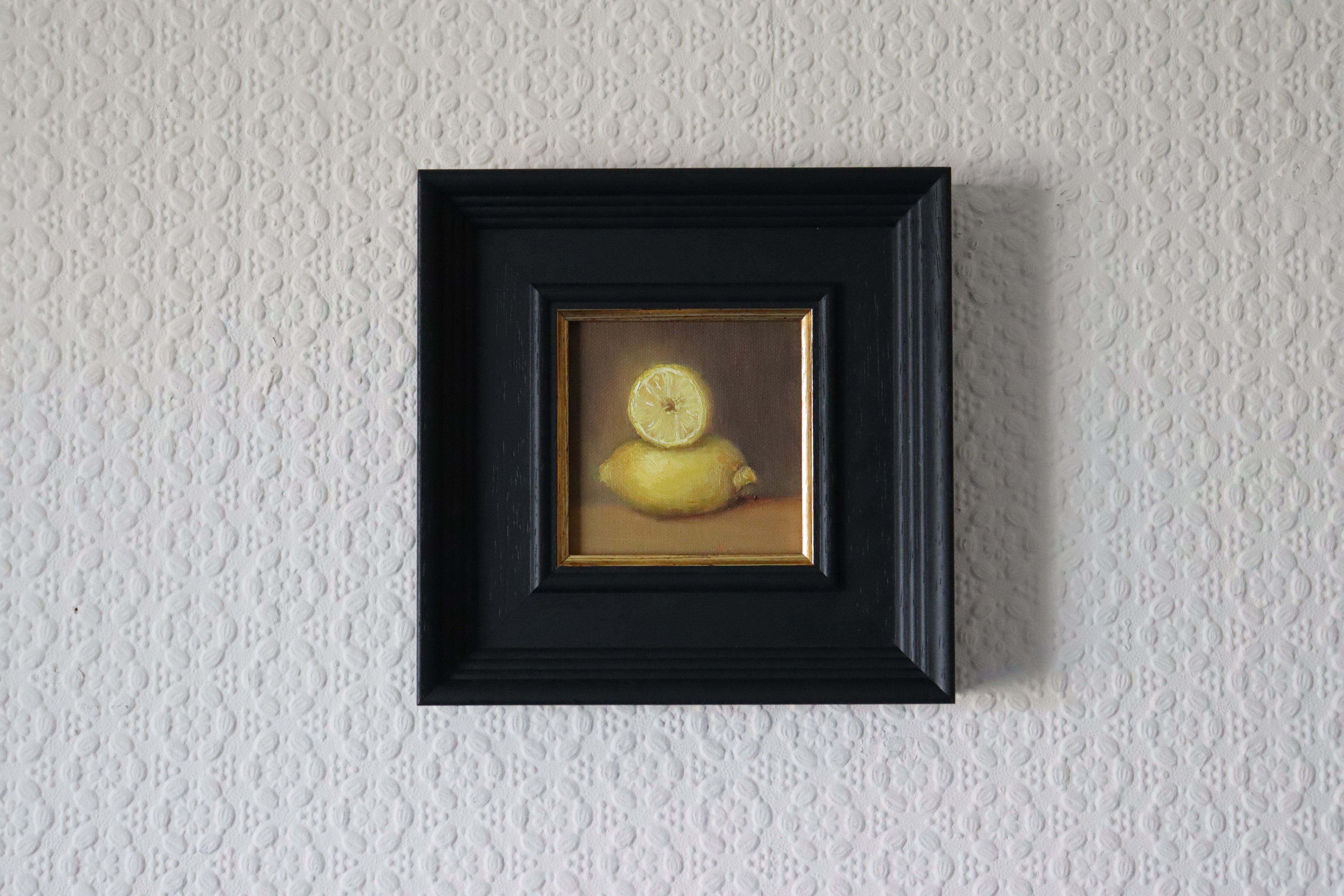 Framed artwork of a lemon on a textured wall. A painting of a very bright lemon with purplish background. Original oil painting of lemons, vibrant citrus still life with humour and warmth by Marta Stolarska
