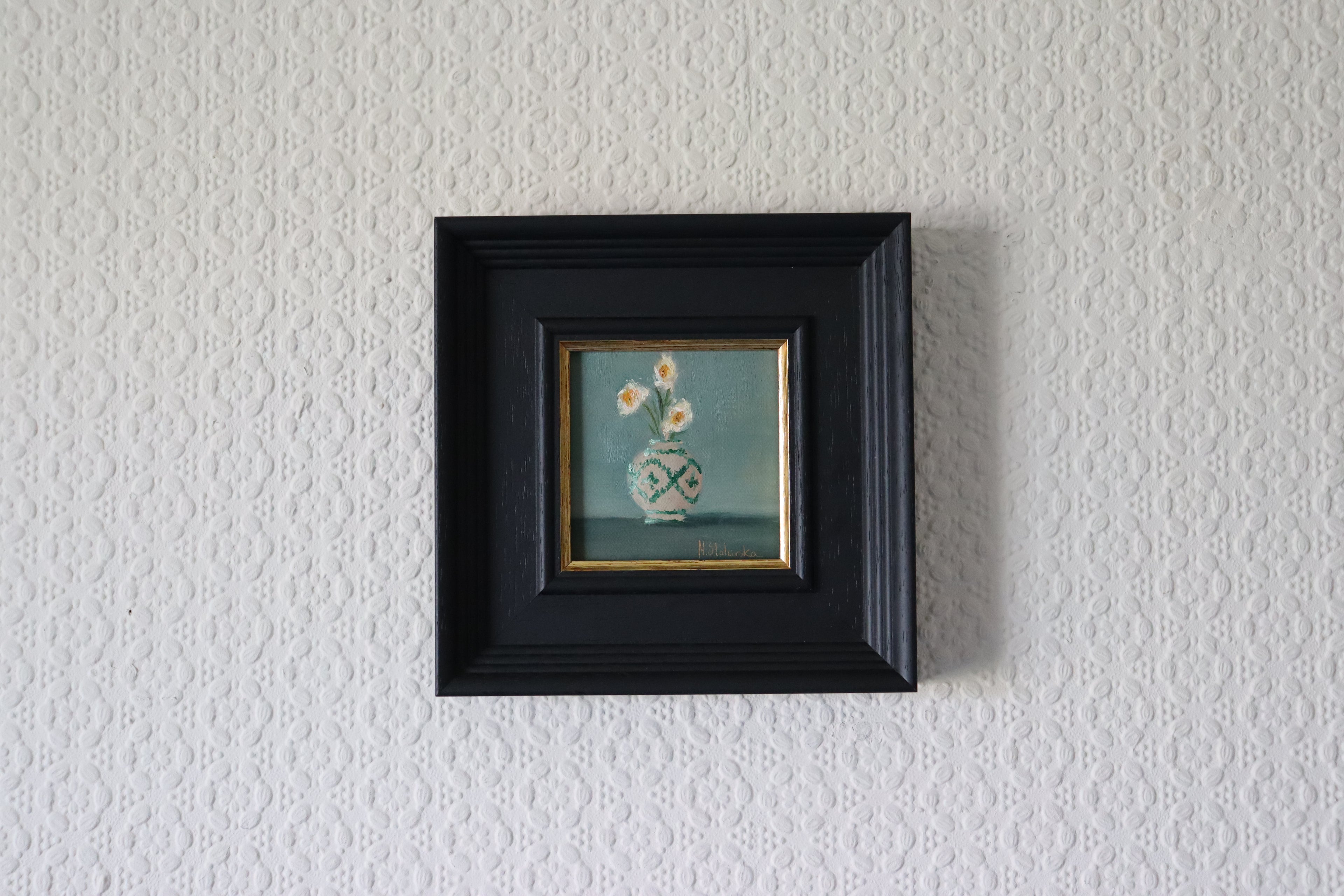 Small framed painting of a vase with flowers on a textured white wall. Original oil still life painting with green design, decorative vessel with green tones by Marta Stolarska