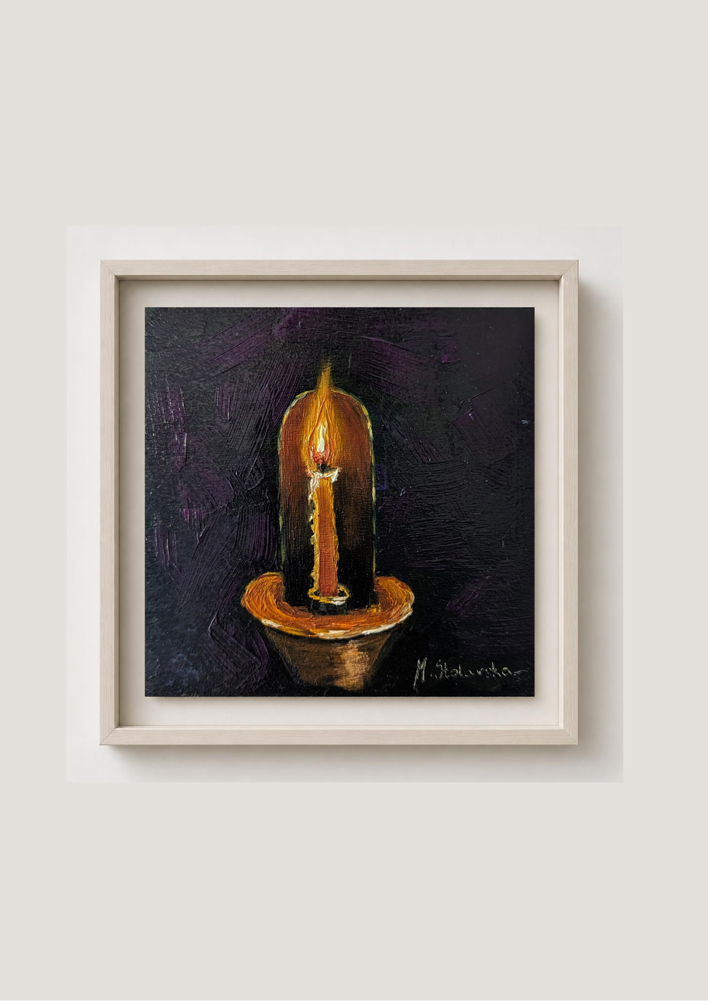 A framed painting of a lit candle on a dark textured background, presented in a light wood frame against a neutral off-white wall.