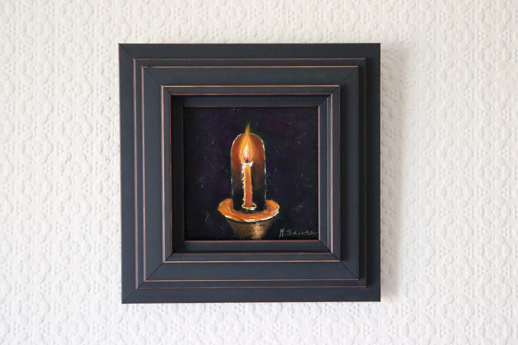 Framed artwork of a candle on a textured white wall. Original oil Painting of a lit red candle on a dark purple background on a cradled panel. 