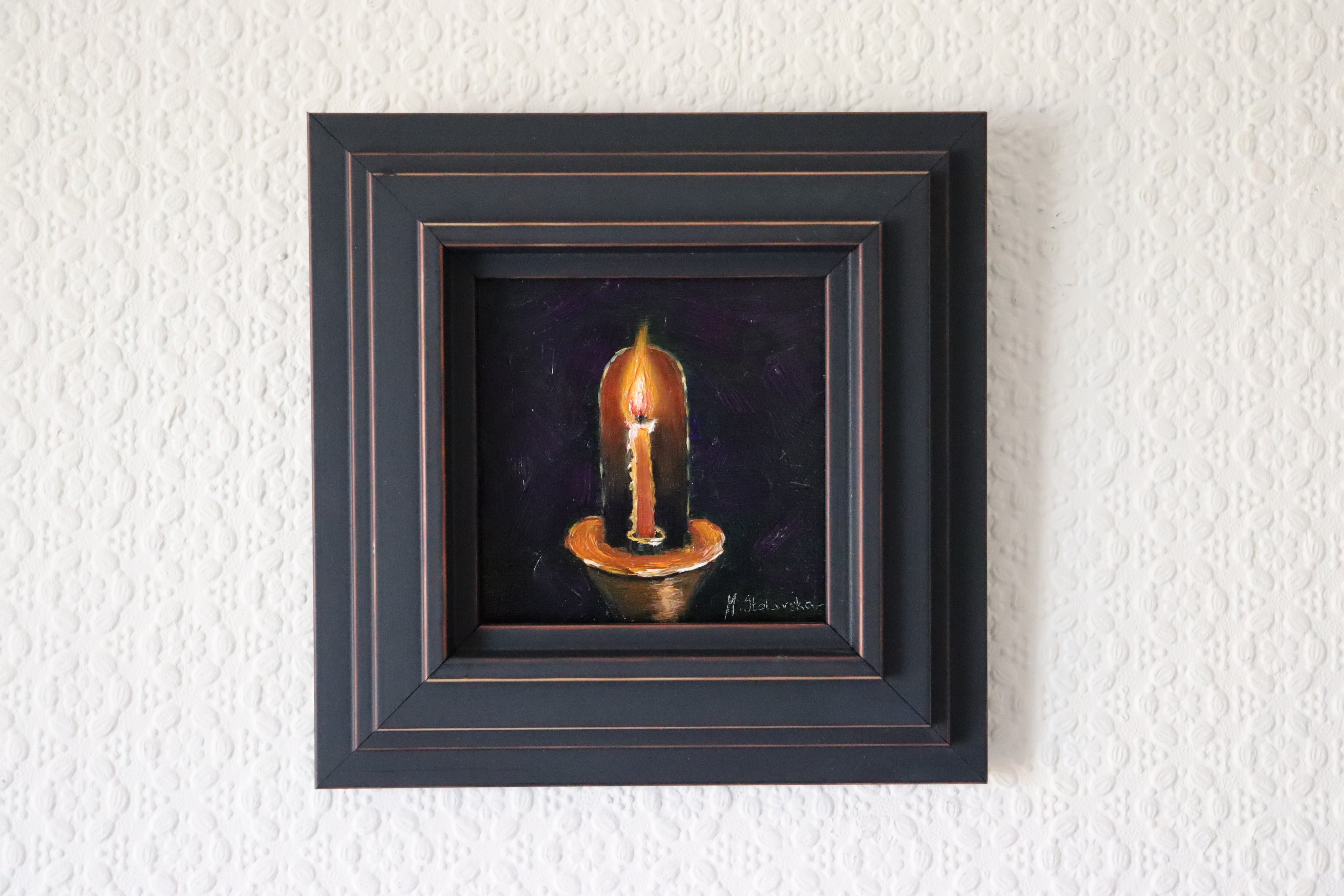 Framed artwork of a candle on a textured white wall. Original oil Painting of a lit red candle on a dark purple background on a cradled panel. 