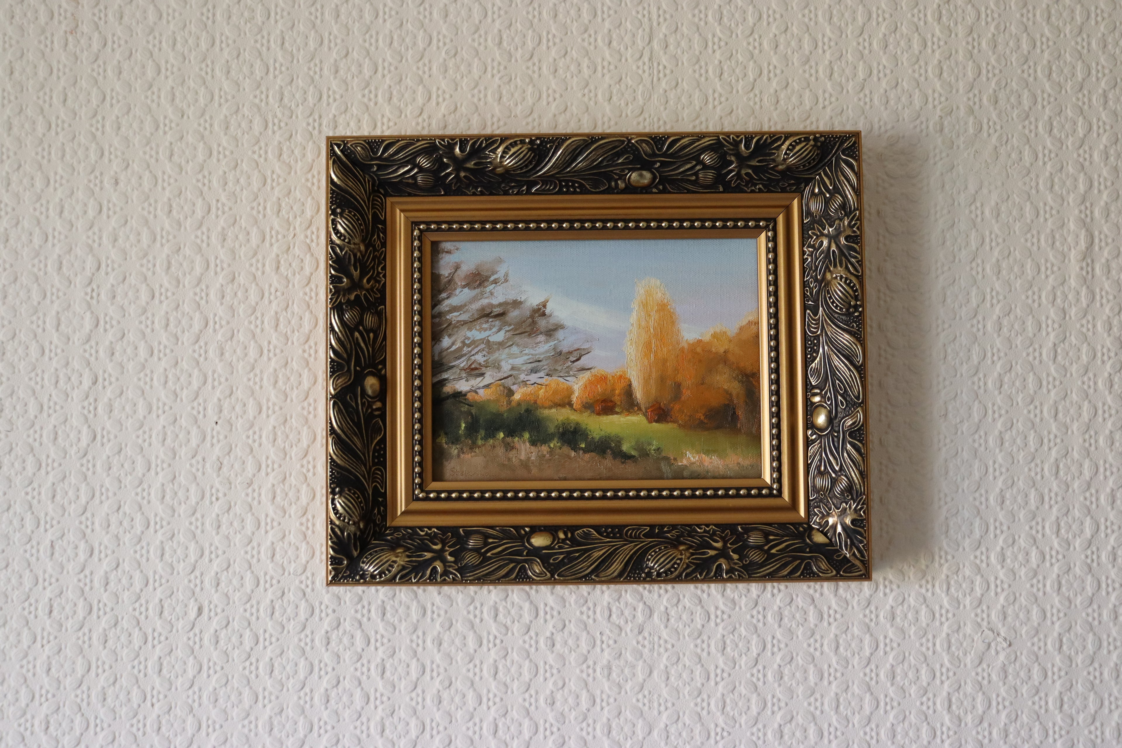 Framed painting of a landscape with trees and sky on a textured wall. Local artist. Original oil painting of sunset at the stables, trees and golden evening light, Suffolk landscape