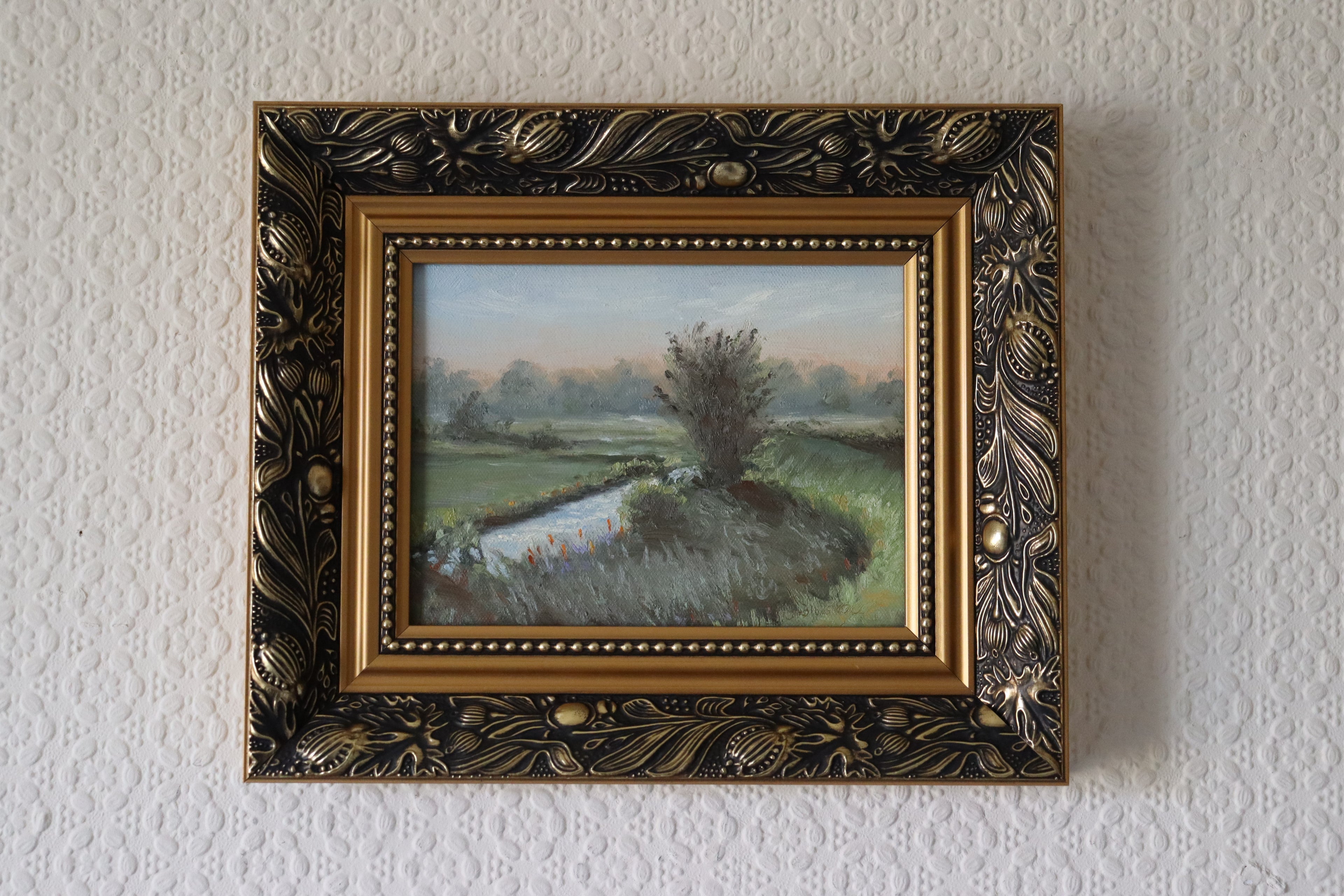 Decorative framed painting of a landscape on a textured white wall. Original painting of Oulton Broads by the Waveney River Suffolk, boats on calm water by a local artist working and living in the area, Marta Stolarska