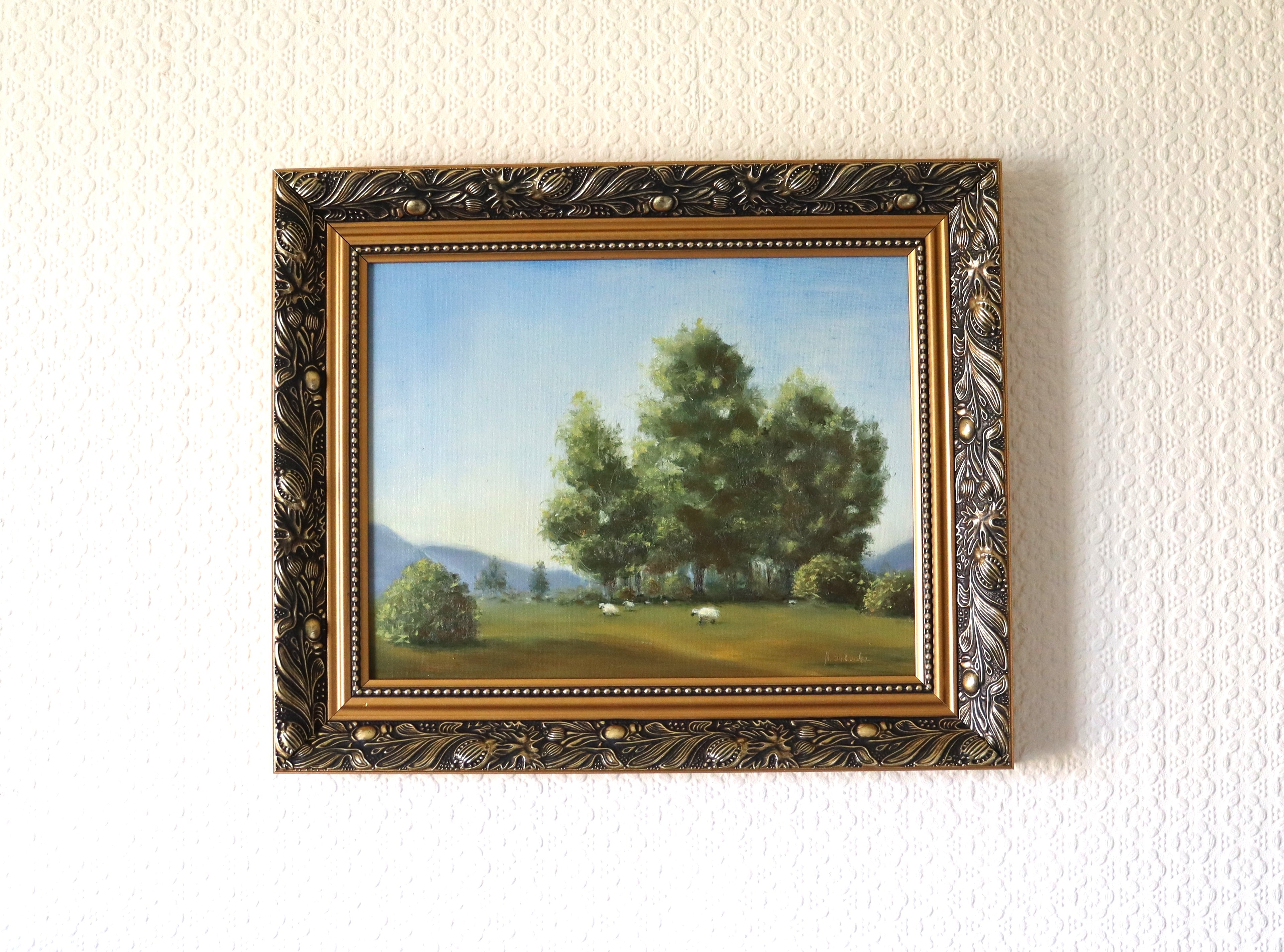 Framed, lifestyle depiction of a painting by a local artist. Original oil painting of tall trees and sheep in Suffolk landscape, painted on a dog walk, golden frame