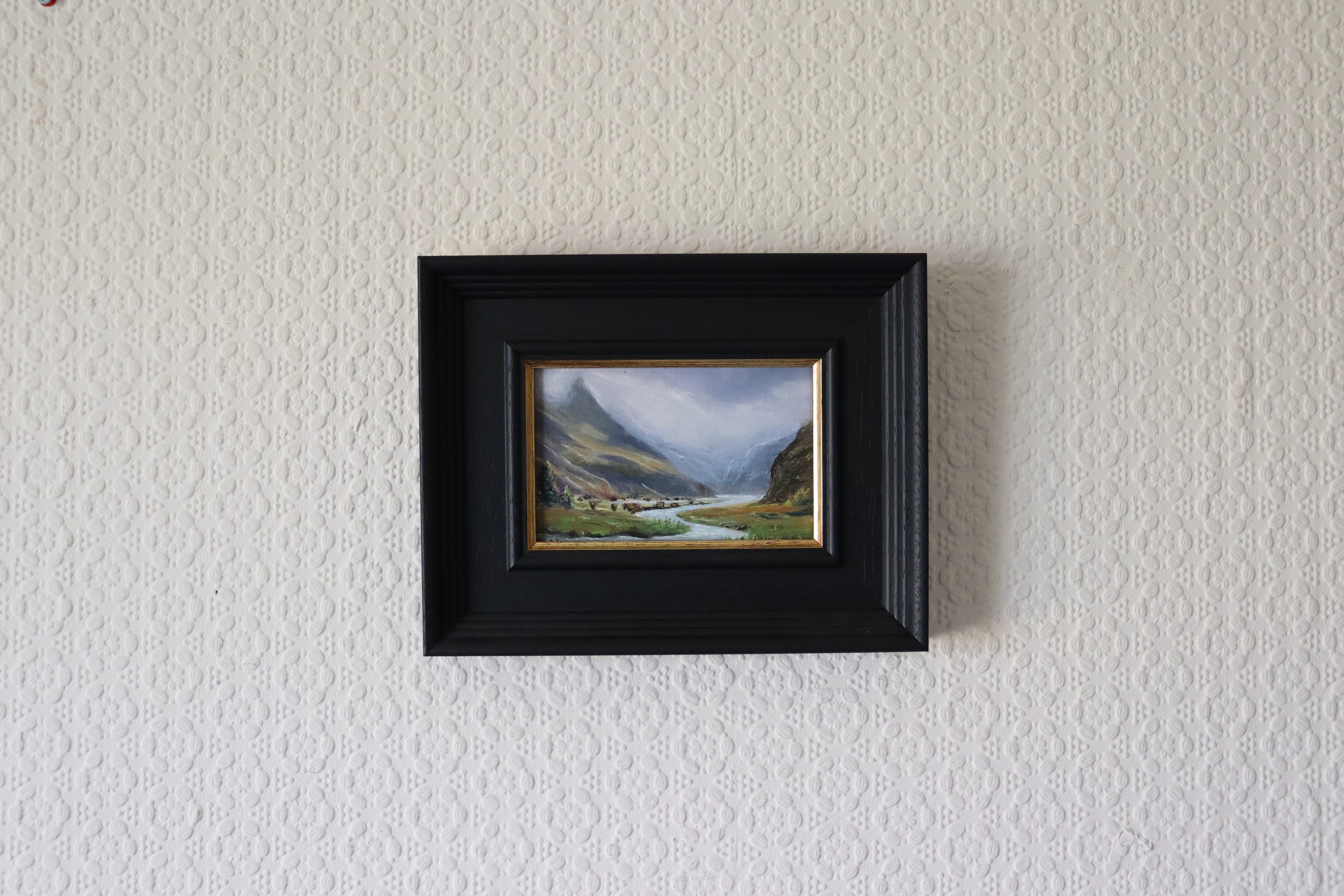 Framed landscape painting on a textured wall. Original oil painting of misty mountains landscape, atmospheric mountain scene in soft mist and cloud