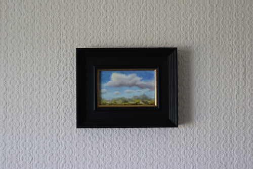 Framed painting of a landscape with clouds on a textured wall. Original oil painting of changing weather over open landscape, dramatic sky with clouds and shifting light