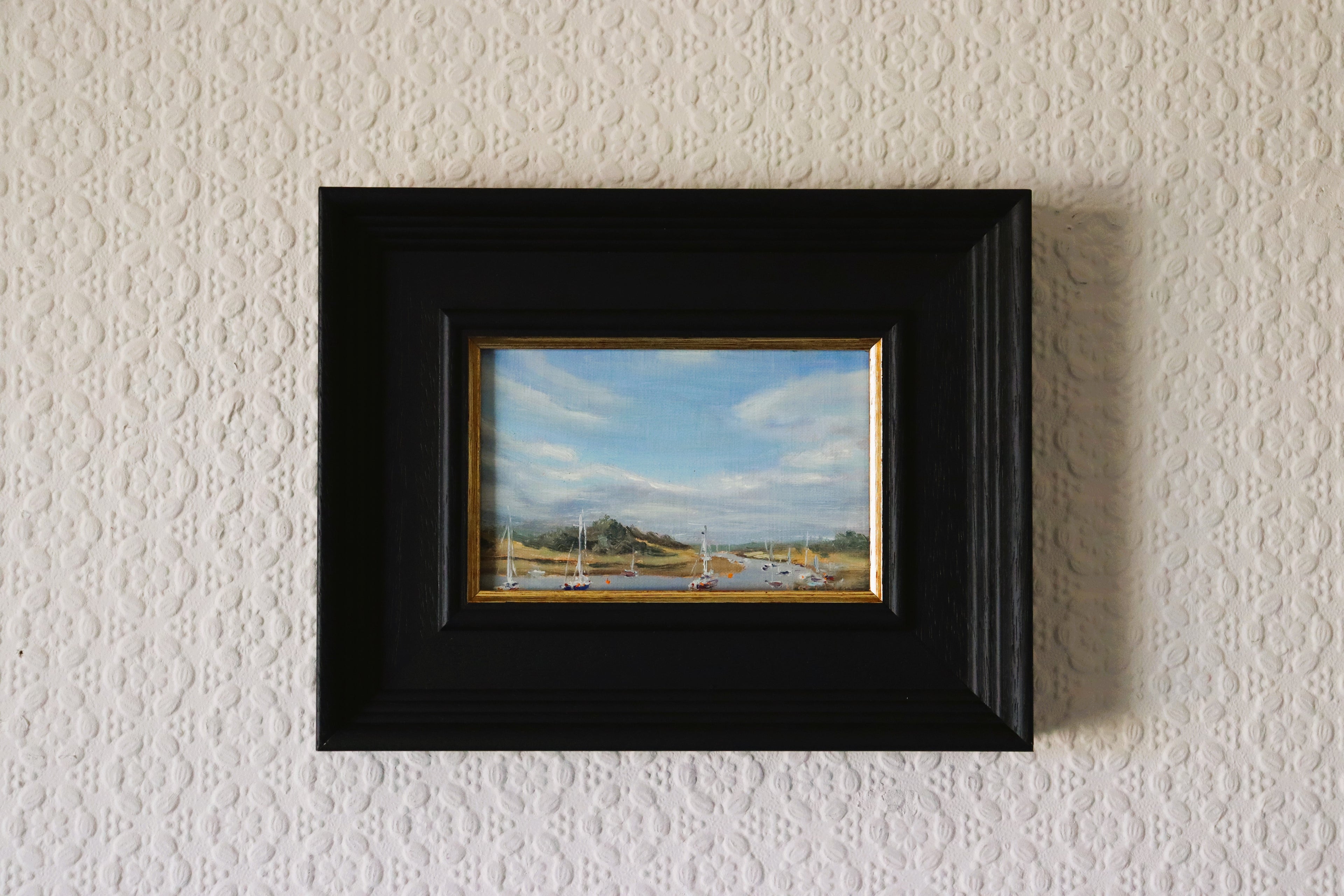 Framed painting of a landscape on a textured wall. Original oil painting of the Norfolk Broads busy with boats, summer scene on the waterways