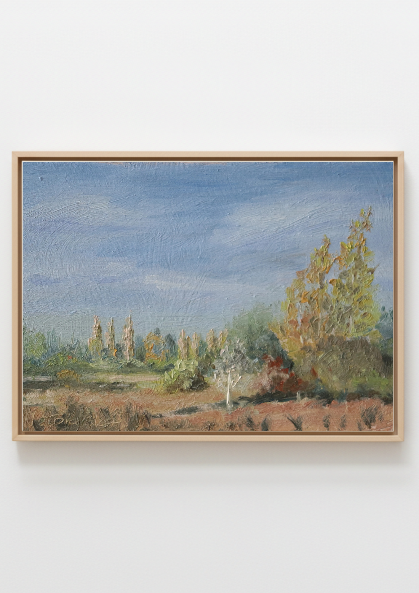 A framed painting on canvas, depicting Scenic landscape with trees and a blue sky. Original oil painting of a path towards the meadows at Carlton Marshes Suffolk, and open fields, hung on a plain white wall.