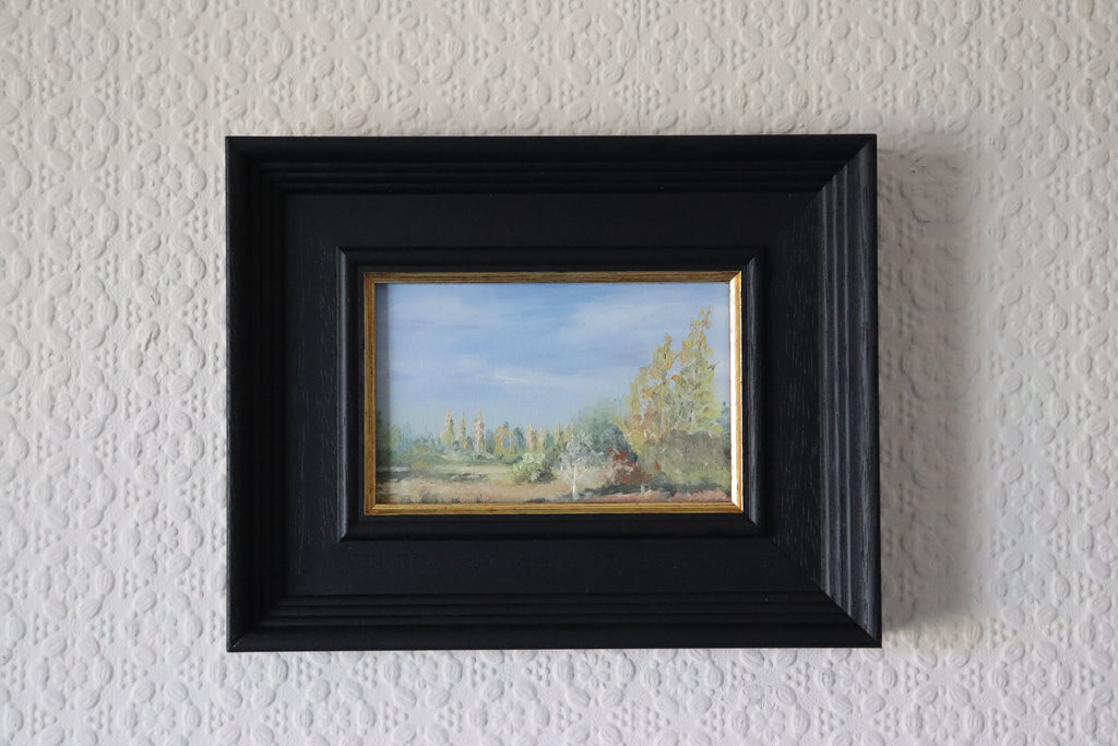 Framed painting of a landscape on a textured white wall. Scenic landscape with trees and a blue sky. Original oil painting of a path towards the meadows at Carlton Marshes Suffolk, and open fields