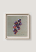 A framed still life painting of a cluster of purple grapes on a muted green-gray background, mounted on a light beige wall.