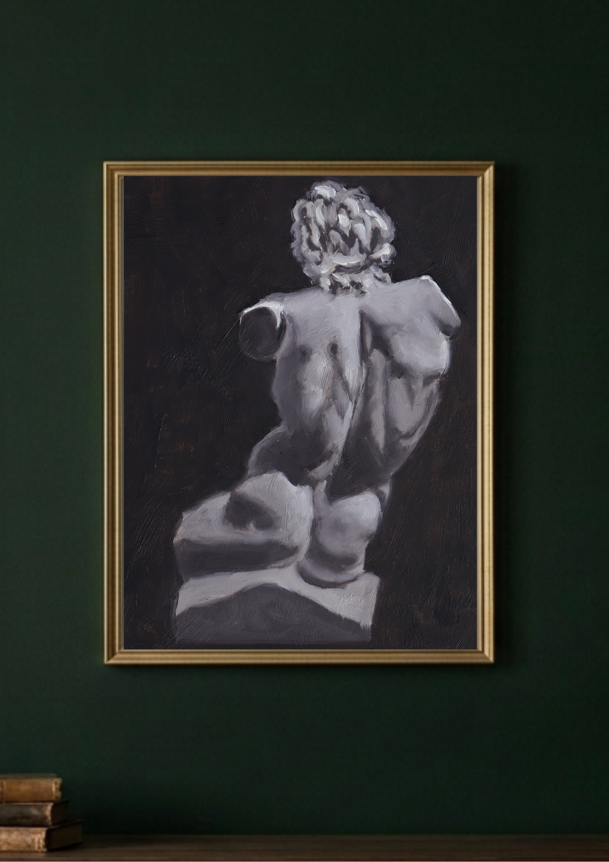 A framed black and white classical sculpture painting hanging on a dark green wall, with a gold frame and a small stack of books at the bottom.