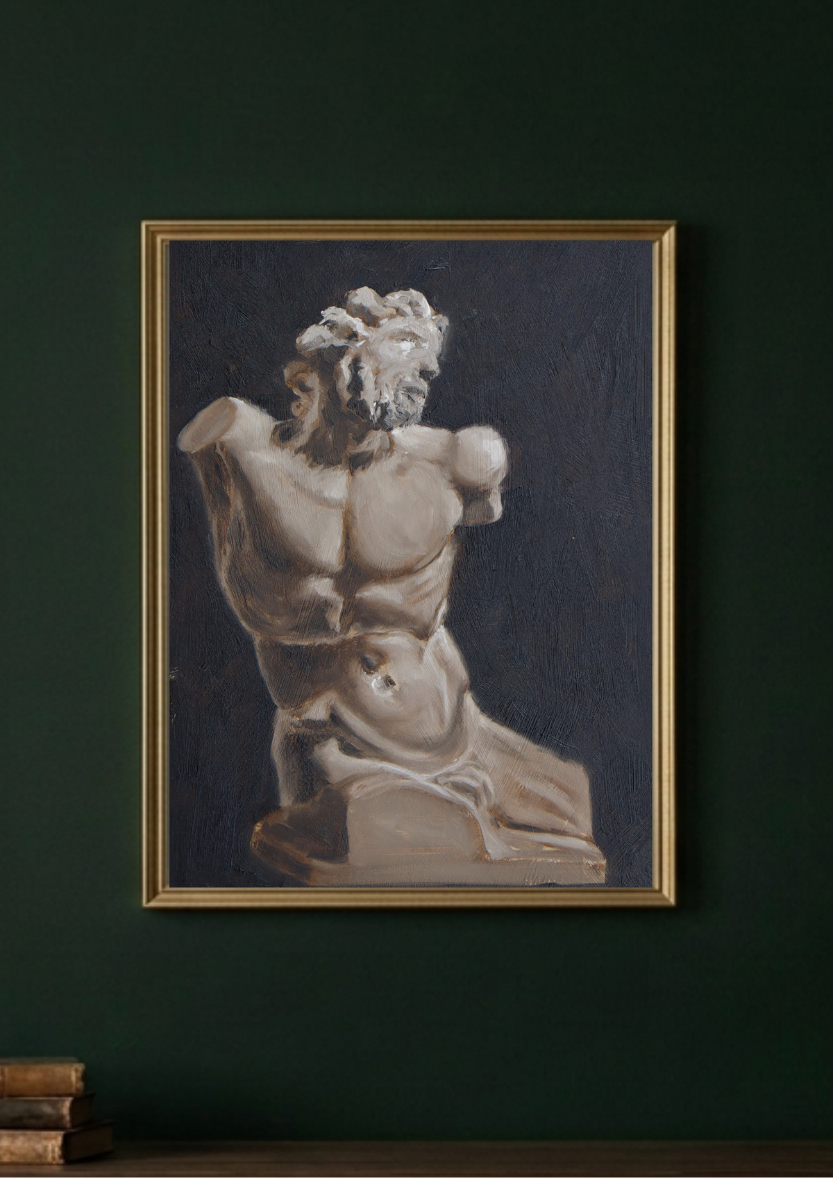 A framed art print featuring a classical sculpture of a muscular male torso against a dark background, hung on a dark green wall above a wooden surface with books.