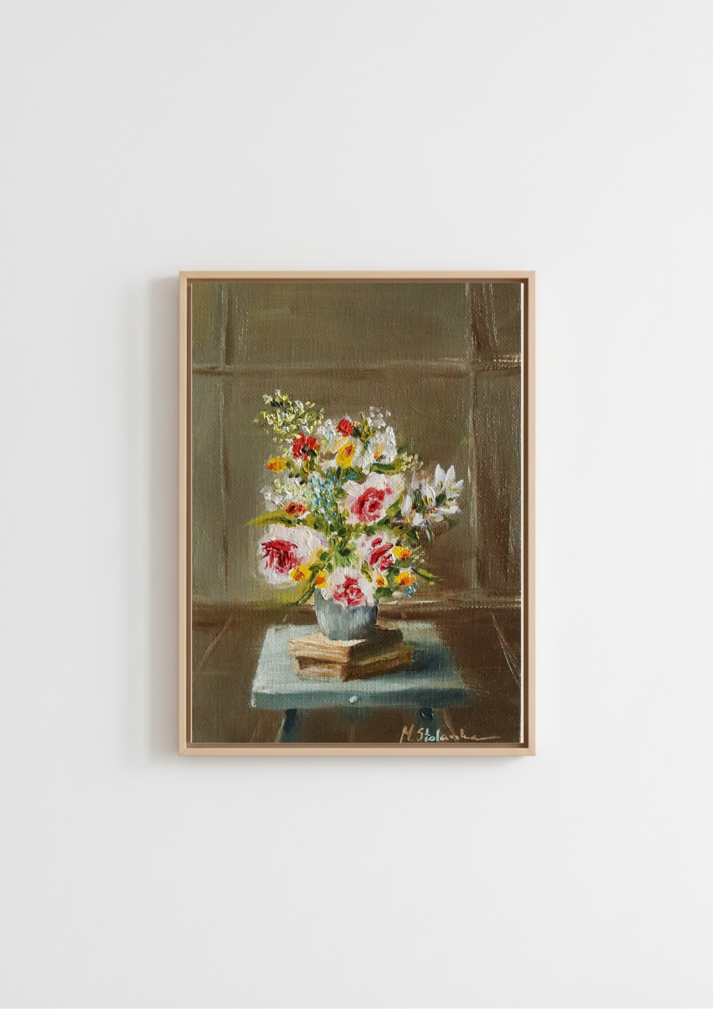 A framed still life painting of a vibrant flower bouquet on a table, hung on a plain white wall. May Abundance - original oil painting by Marta Stolarska, an overflowing spring bouquet of pink roses and white flowers in a vase on a taboret with notebooks, painted from life on handmade linen board, 10 x 15 cm