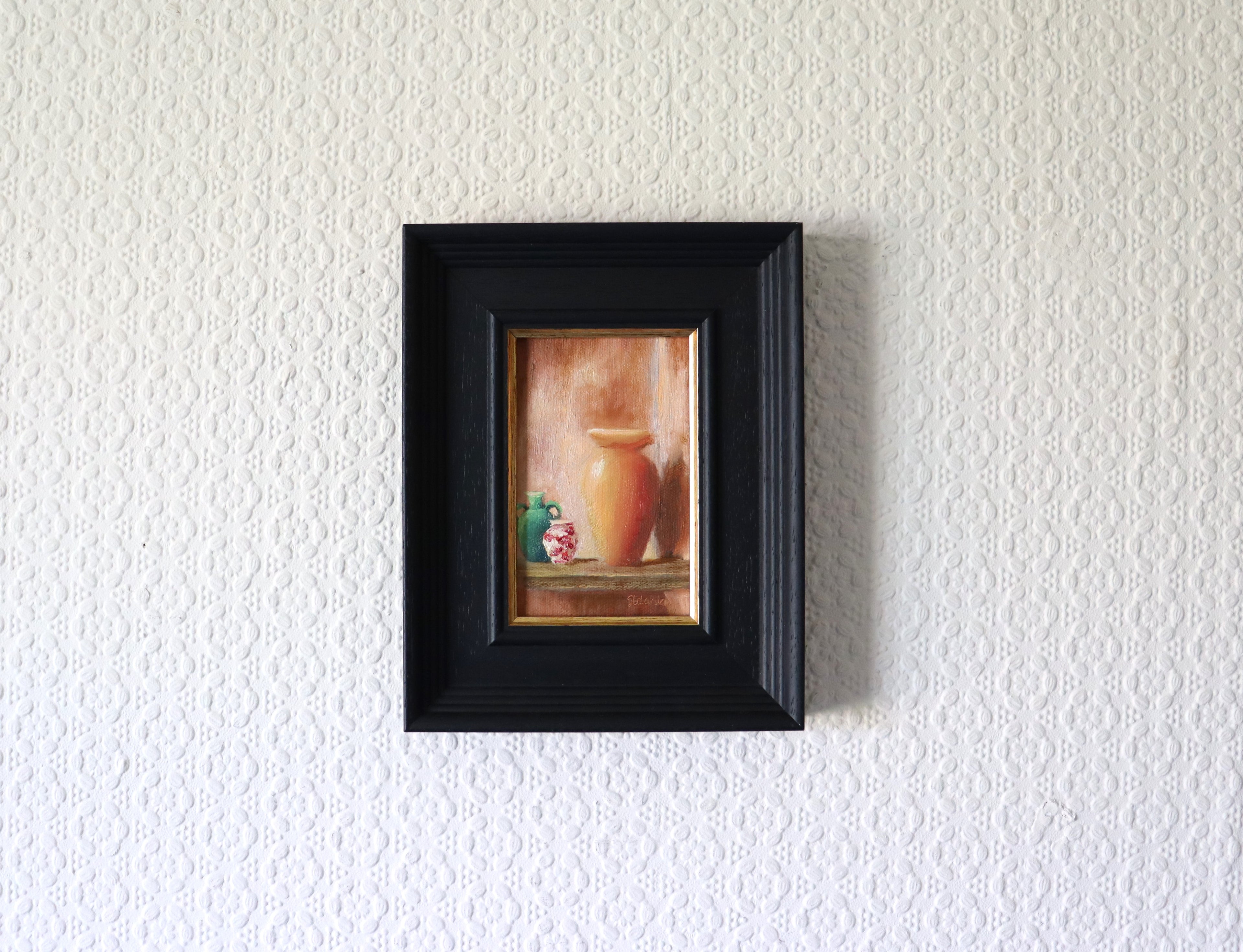 Framed artwork of a vase on a textured white wall in a lifestyle setting. Original oil still life painting of Mediterranean pottery in warm golden light, terracotta and ceramic vessels