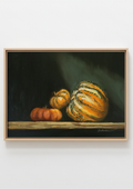 A framed still life painting depicting three pumpkins on a wooden surface against a dark background, shown hanging on a light gray wall. Still life painting with a copper kettle  and pumpkins on a dark background. Chiaroscuro sculptural techniques.