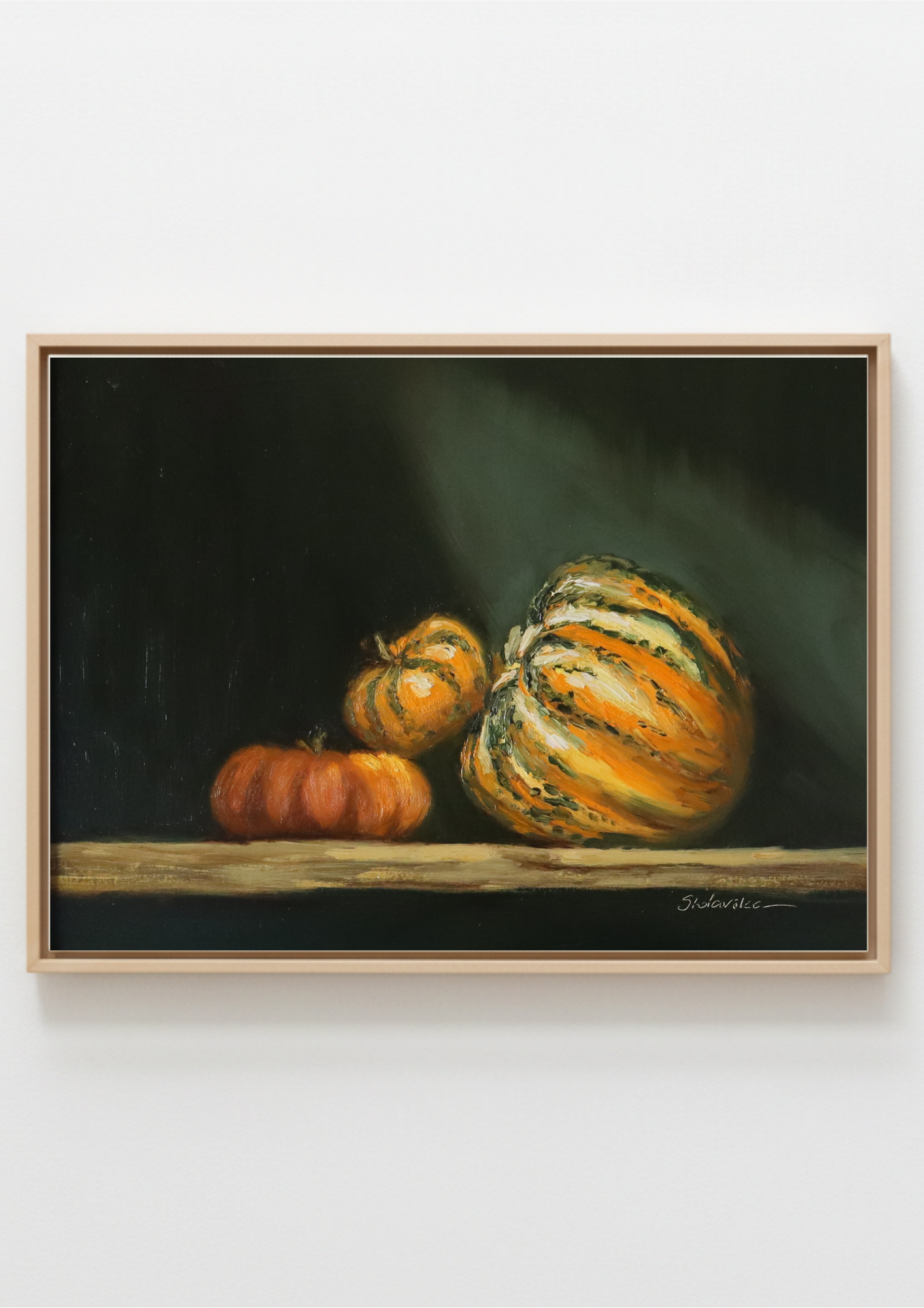 A framed still life painting depicting three pumpkins on a wooden surface against a dark background, shown hanging on a light gray wall. Still life painting with a copper kettle  and pumpkins on a dark background. Chiaroscuro sculptural techniques.