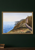 A framed landscape painting of a coastal cliffside path leading to a small stone hut, displayed on a dark green wall above a wooden surface with books.