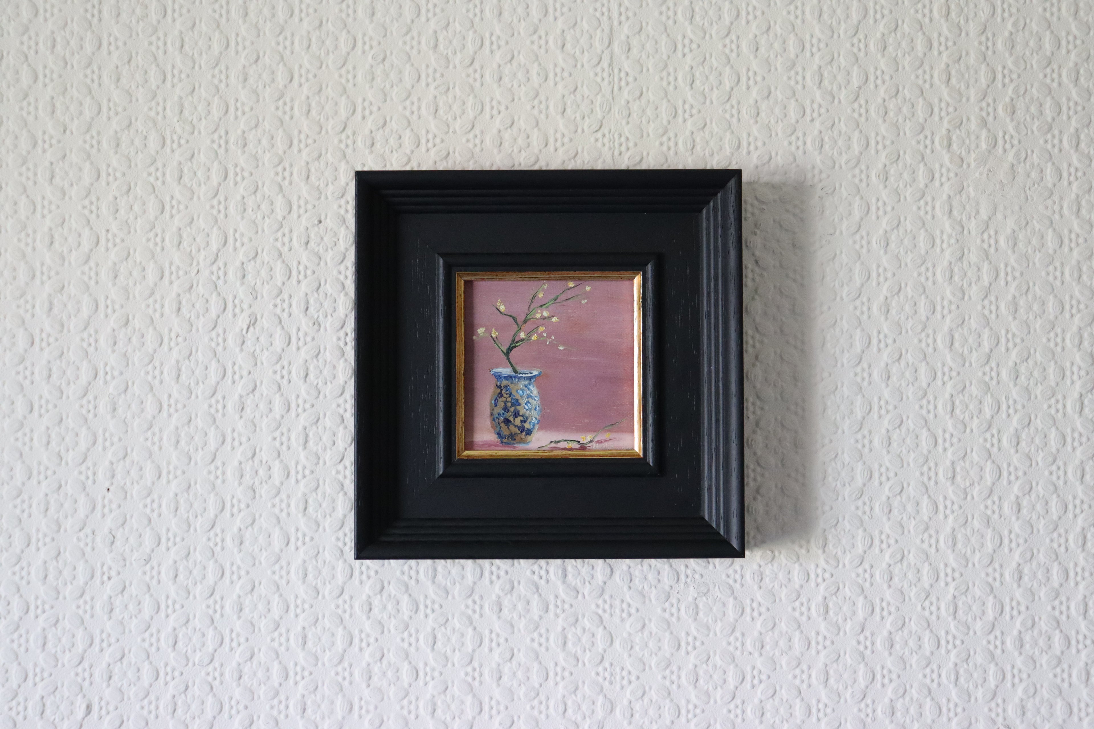 Small painting of a vase with branches in a black frame on a textured white wall Original oil painting of Sparkly Joy, sparkling blue vase with yellow flowers catching the light