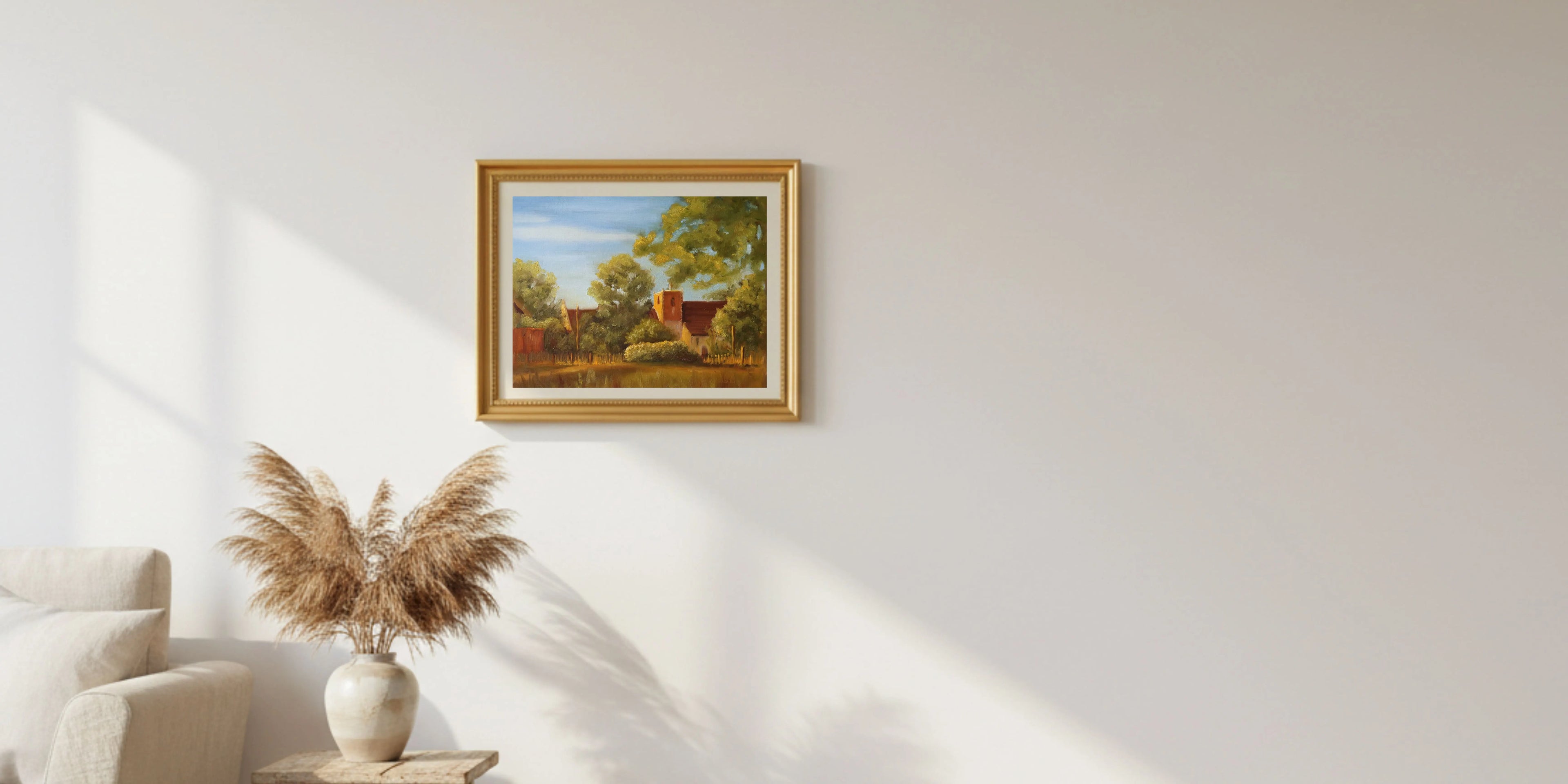 Framed painting of a landscape, St Michaels Church In Oulton Broads, part of the Suffolk broads, by Marta Stolarska, on a white wall with a decorative plant and chair in the foreground.
