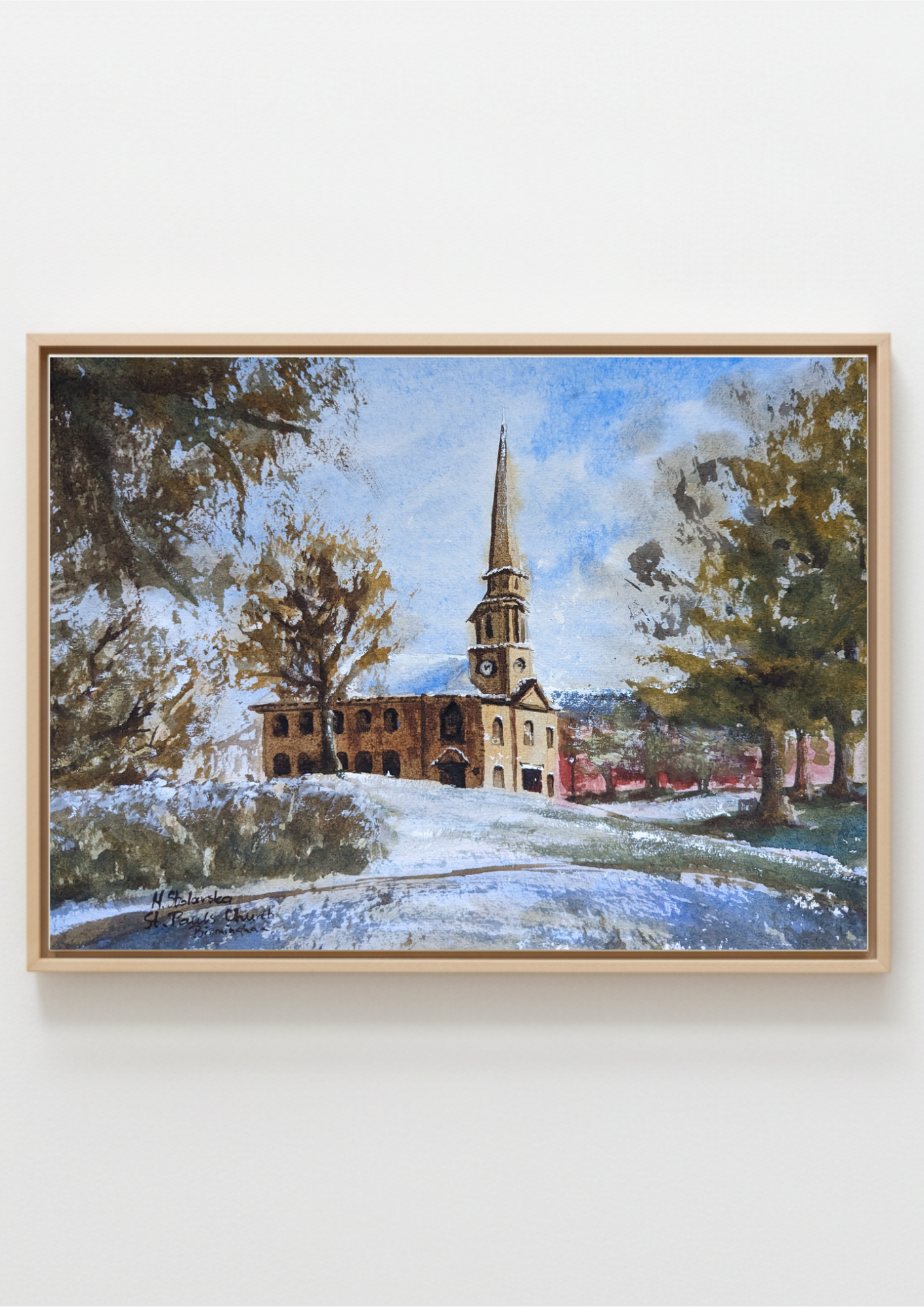 A framed watercolor painting of a church with a tall steeple, surrounded by trees and a snowy foreground, displayed on a light gray wall. Local artist.Original watercolour painting of St Paul's Church Birmingham Jewellery Quarter on a cold bright winter day