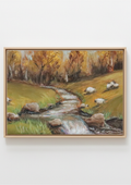 A framed landscape painting depicting a winding stream flowing through a grassy field with grazing sheep and autumn trees, shown against a plain light gray background. Framed painting of a landscape with trees and a stream on a textured white wall. Original oil Painting of a landscape with sheep, trees, and a stream and beautiful autumnal colours and trees. Water has a multitude of pastel colour twinkling gently.