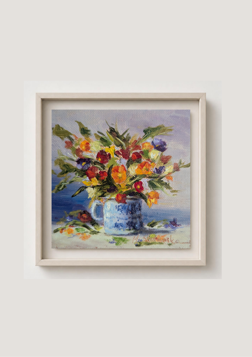 A framed still life painting of a vibrant flower bouquet in a blue-and-white vase, hung on a light beige wall.